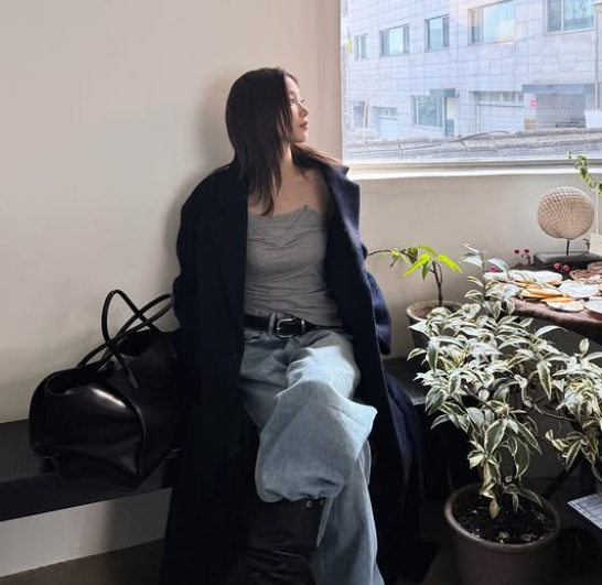 회색 슬리브 이너와 와이드진을 입고 네이비컬러 울코트를 걸친 채 창가에 앉은 카즈하의 데이트룩